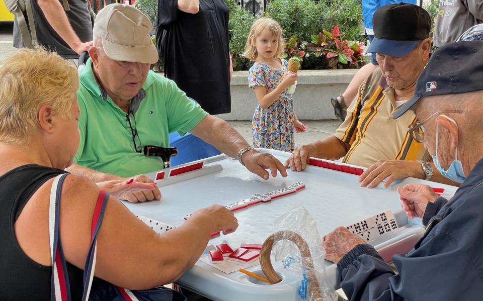 Photograph of 4 older adults playing dominos while a young girl watches